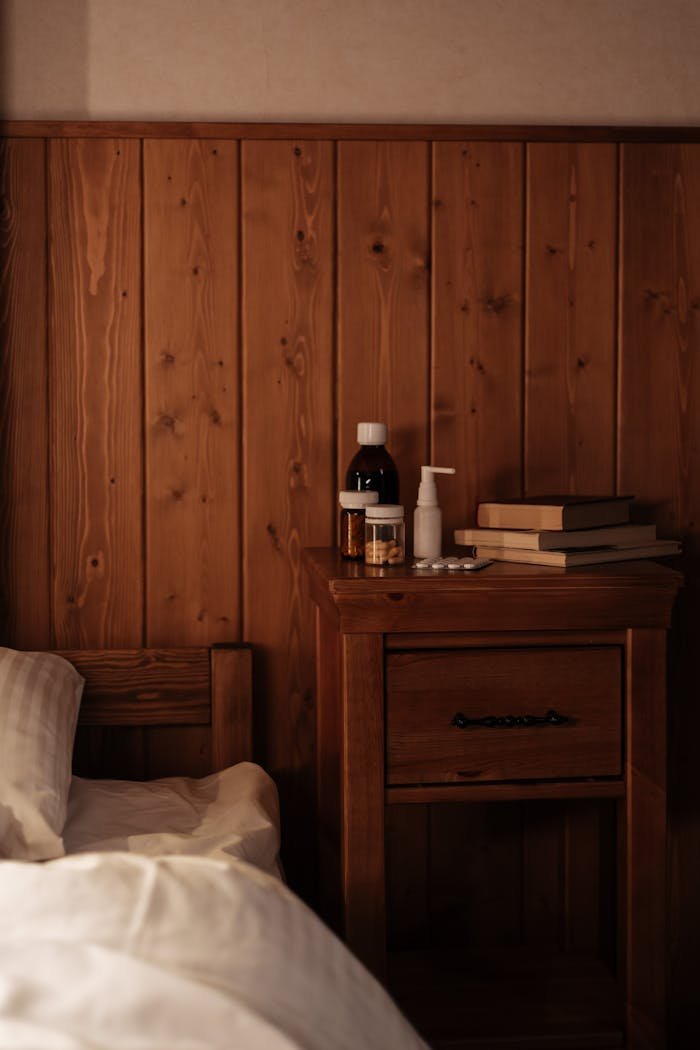 Warm wooden nightstand with meds and books, offering a cozy indoor setting.